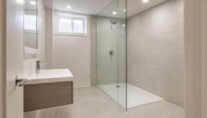 Finished basement bathroom with a curbless glass shower, large-format light tile, floating vanity and a small high basement window