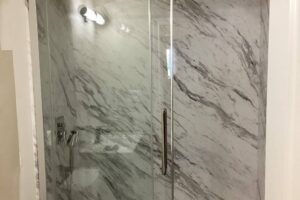 Walk-in shower with marble-look acrylic walls, a glass door and a hand shower